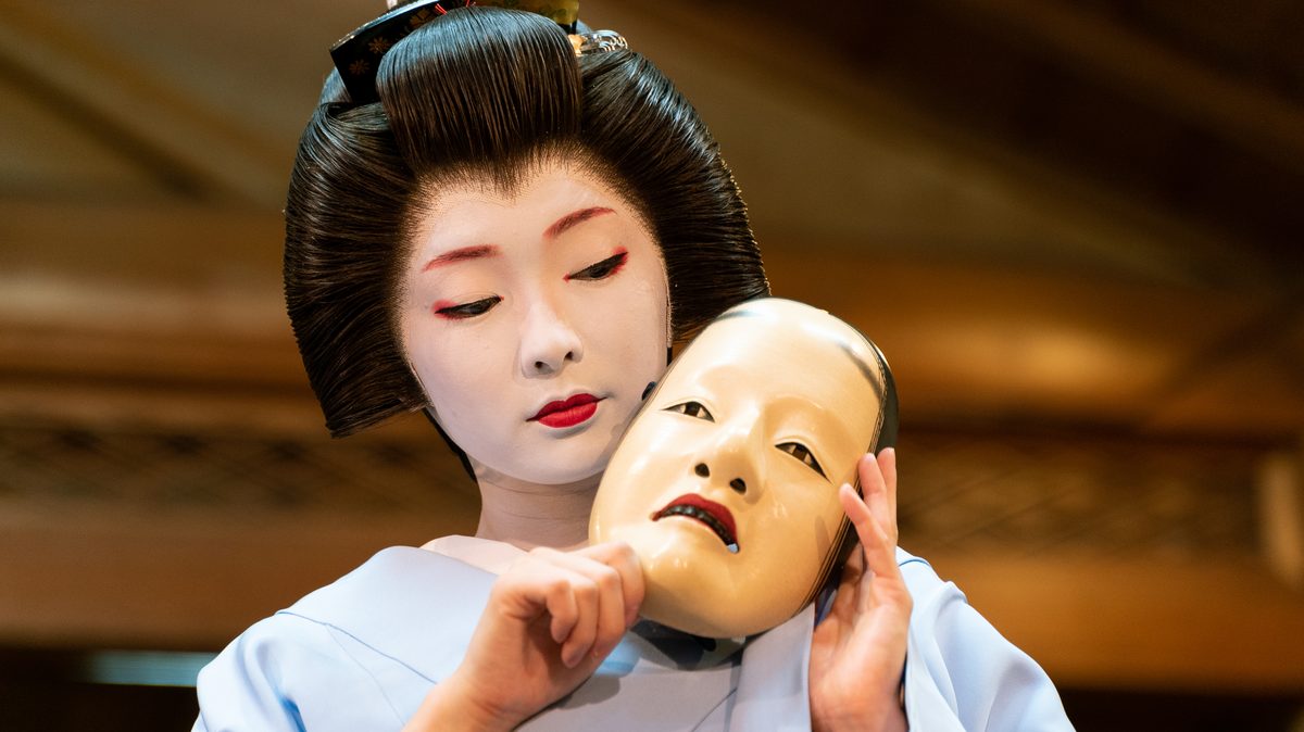 Person holding a traditional Noh mask showing the carved wooden face
