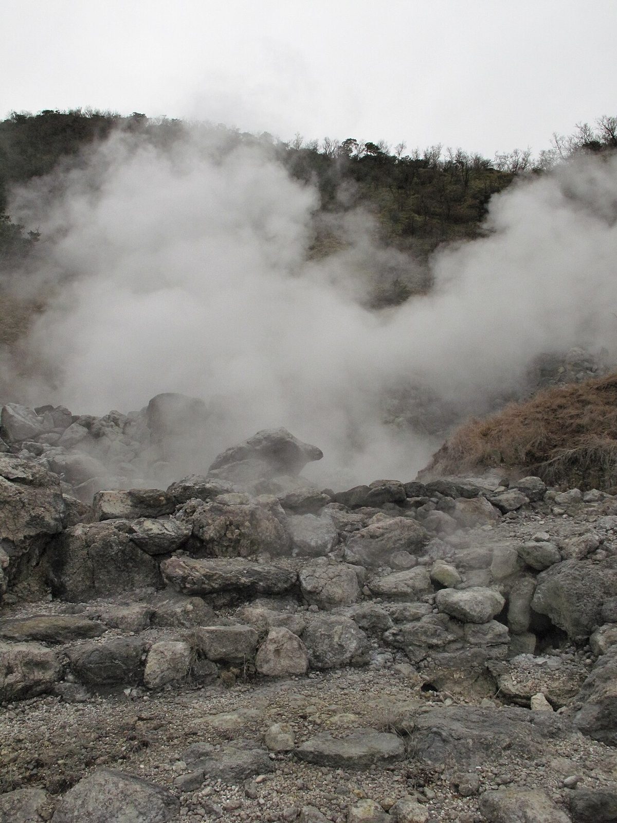 Unzen Jigoku steam vents with barren rocky terrain and surrounding hills